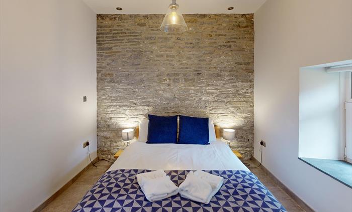 A double bed with deep blue cushions and a geometric throw, set against a rustic stone wall in a peaceful bedroom.